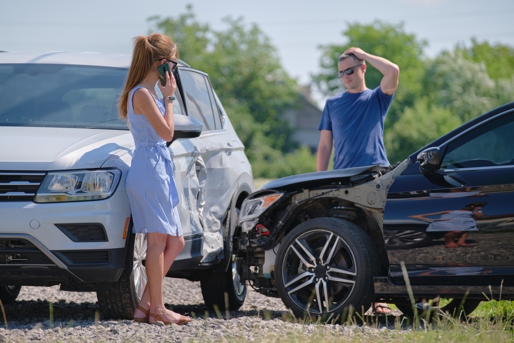 Two drivers on the phone beside damaged cars symbolizing automotive accidents - Pigott Law Group